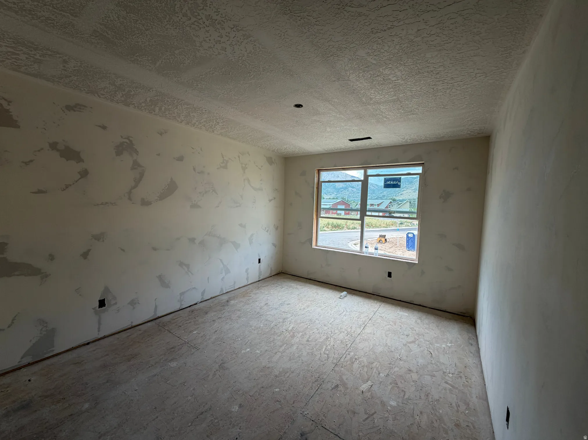 Room featuring a large window, textured ceiling, and unfinished walls and subflooring