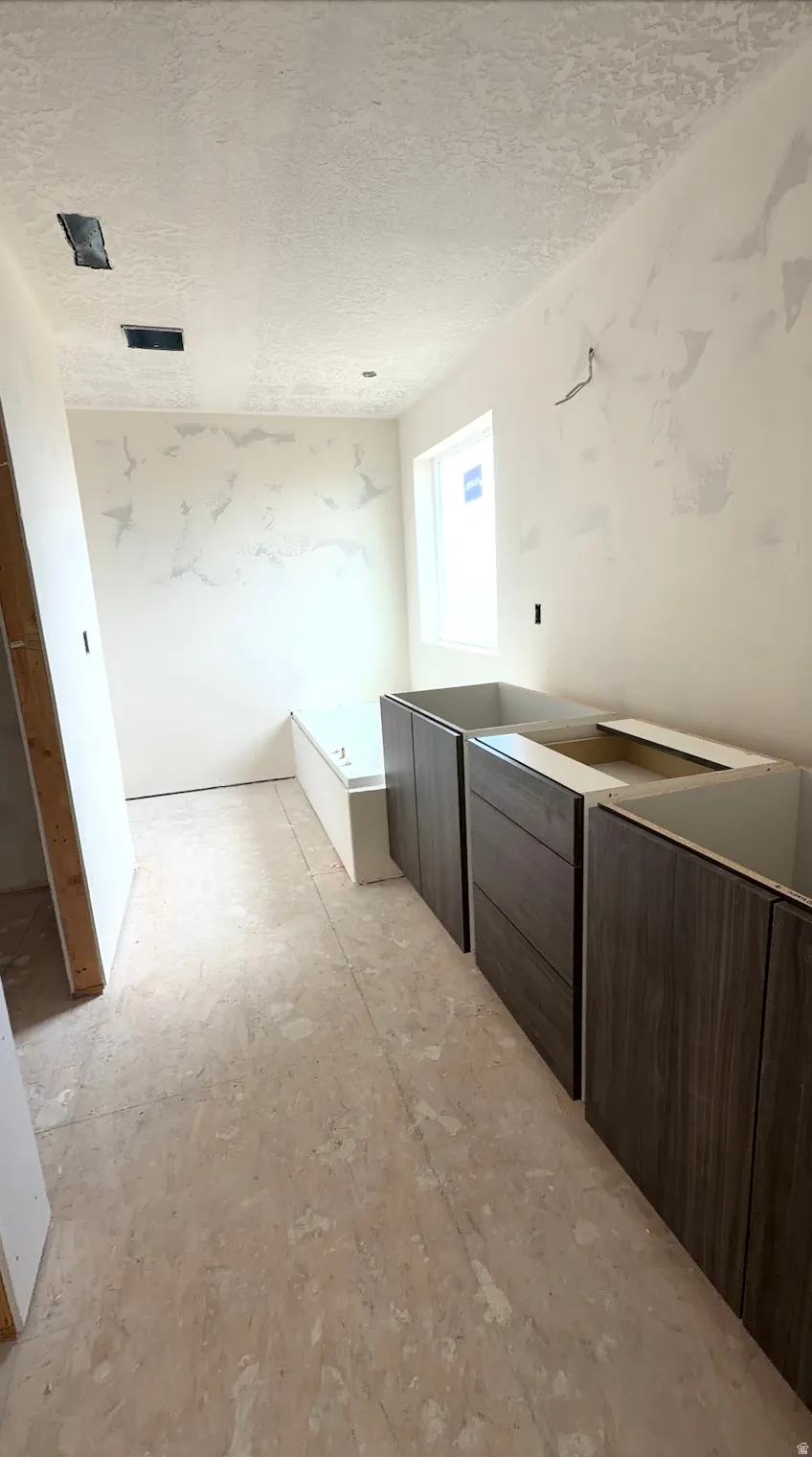 Bathroom under construction featuring wood-finish cabinetry, a window with natural light, and a built-in tub
