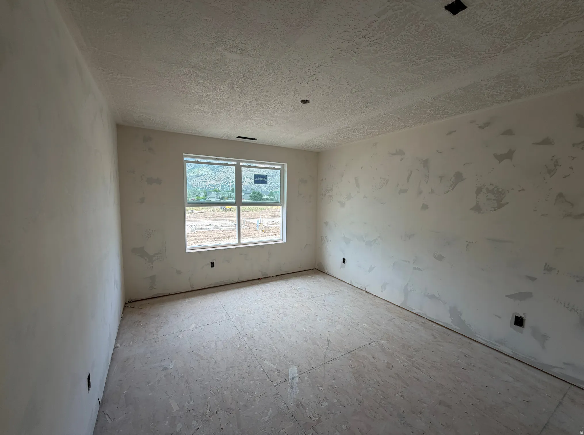 Room under construction featuring a large window with mountain scenery, textured ceiling, and unfinished walls