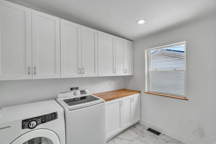 Laundry room featuring white shaker cabinetry, wood-finish countertop, and a window with wood trim