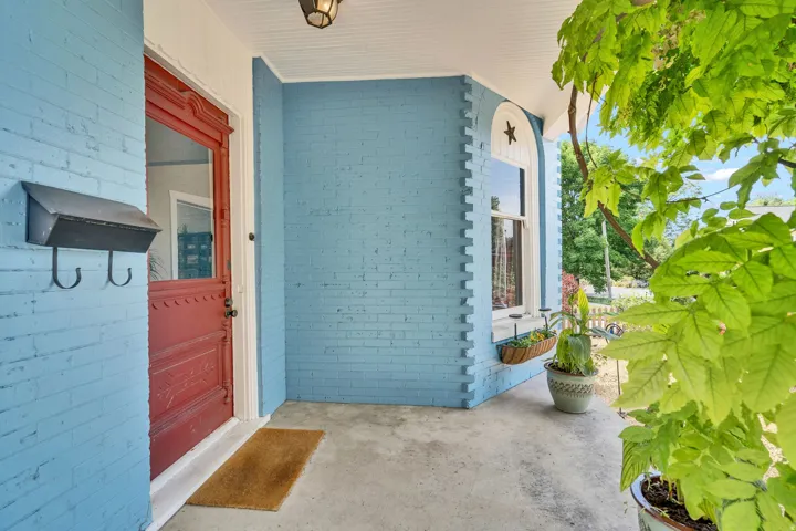 Covered porch entry featuring a decorative red door with glass panel, blue painted brick exterior, and a single arched window with white trim