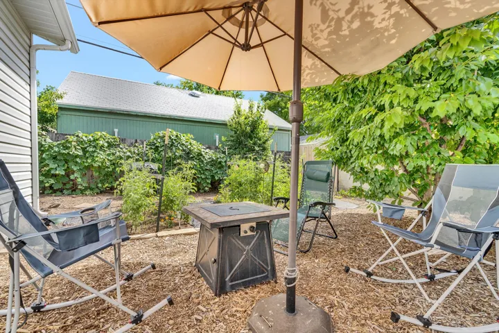 Backyard patio area featuring wood chip ground cover, mature landscaping, and an adjacent building with horizontal siding
