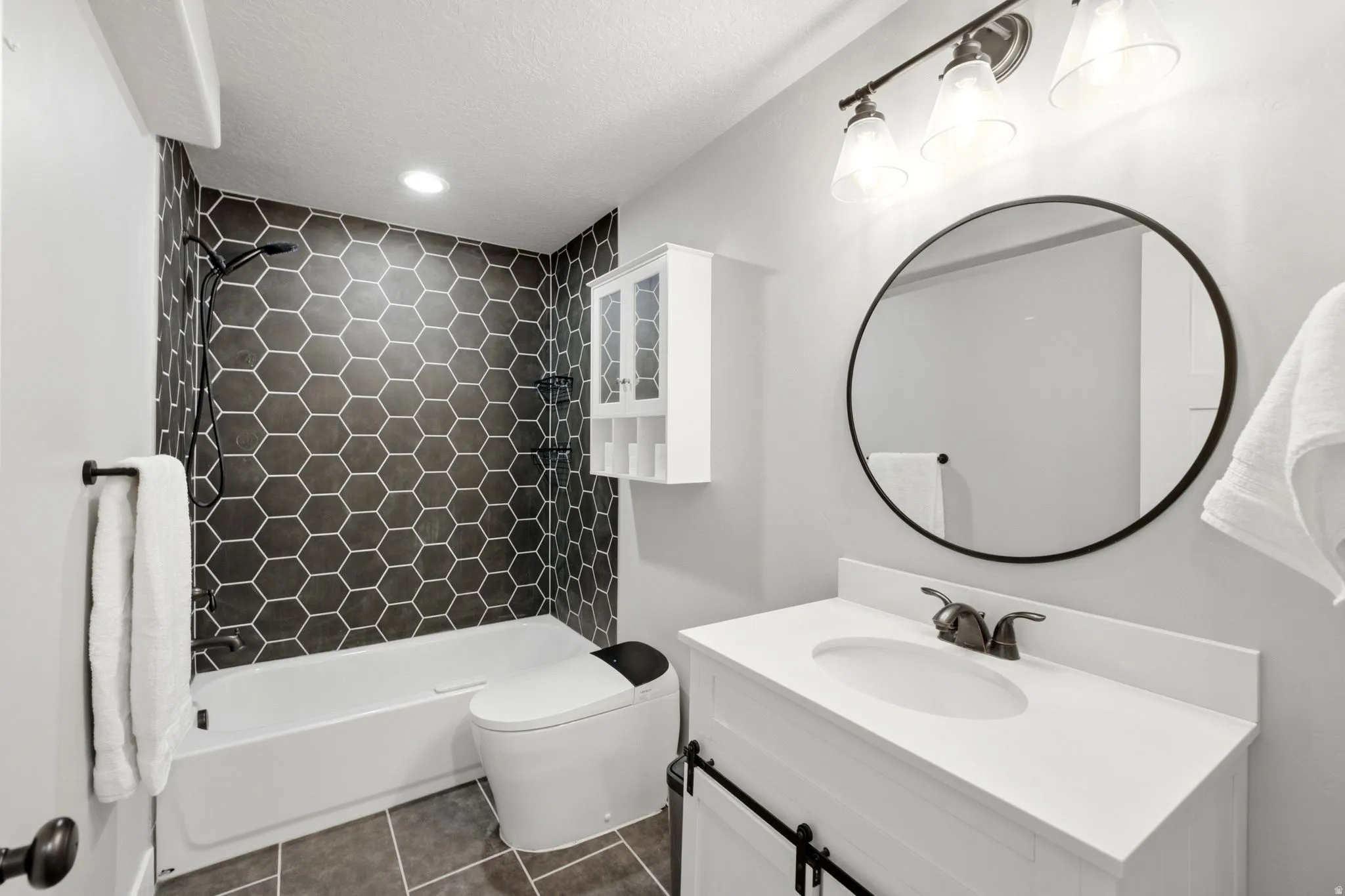 Bathroom featuring a white vanity with a white countertop, a black-framed circular mirror, and a three-light vanity fixture