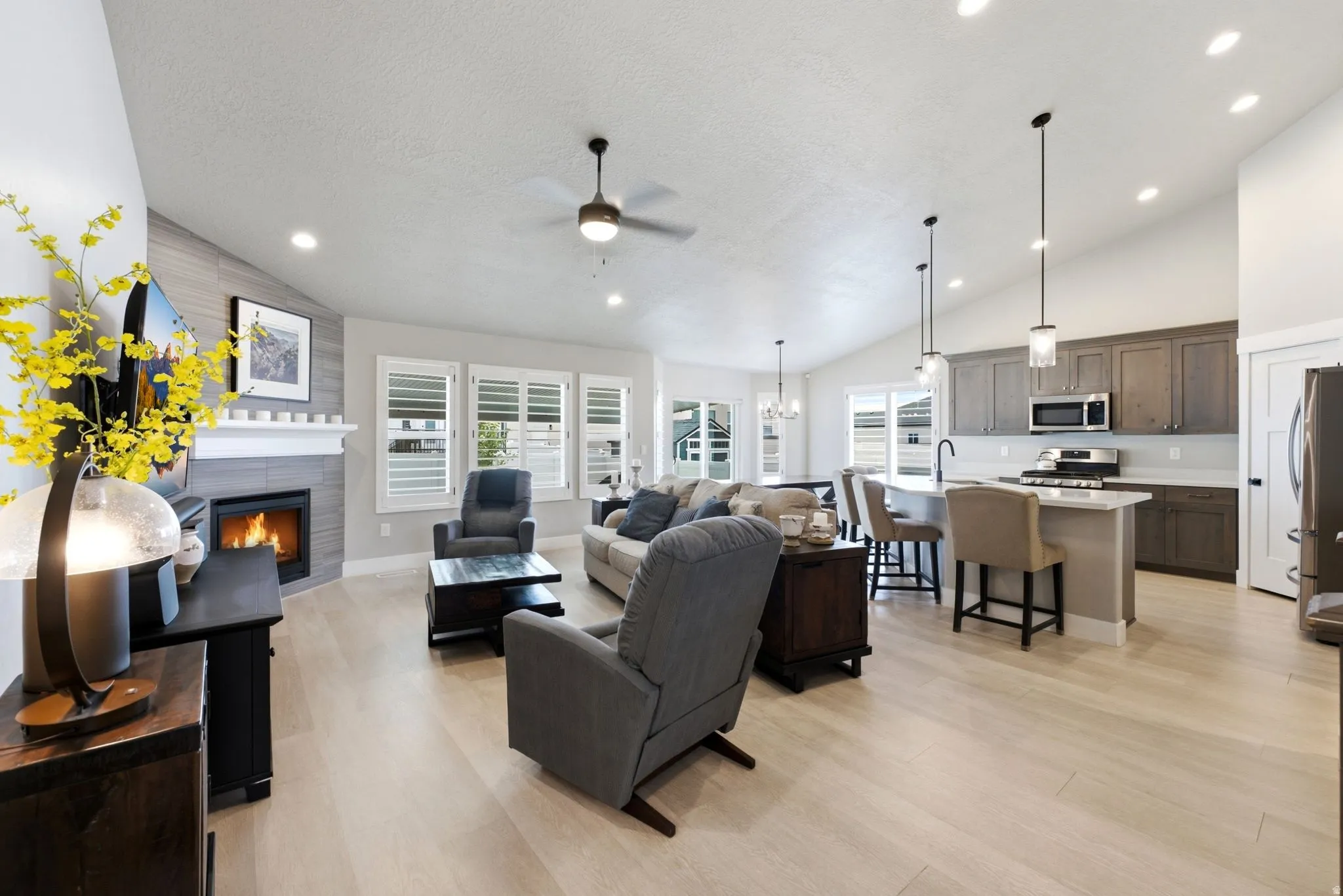Open-concept living space featuring wood-finish flooring, a contemporary fireplace with a tiled surround, recessed lighting, and vaulted ceilings