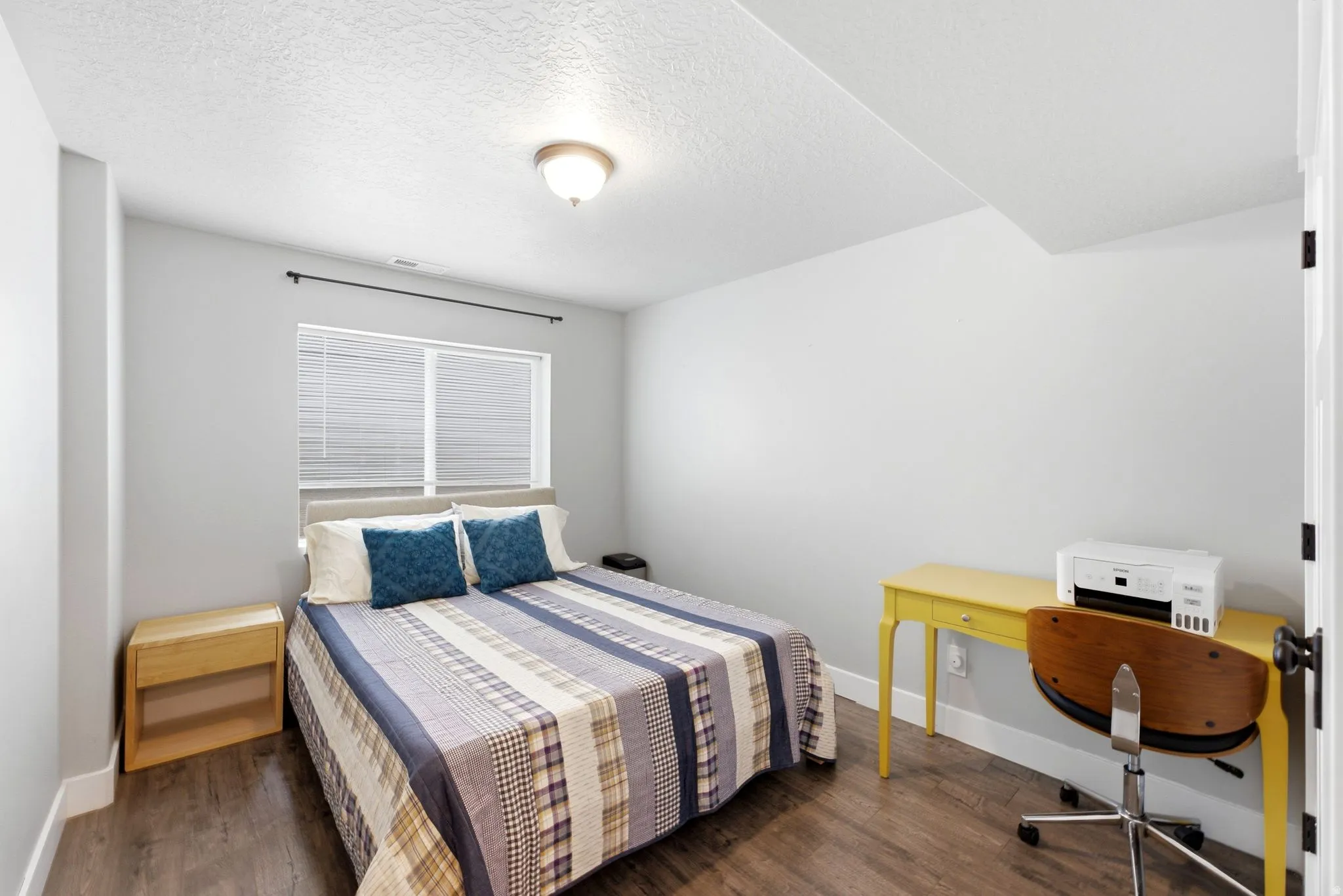 Bright room featuring wood-finish flooring, a window with horizontal blinds, and a flush-mount ceiling light fixture