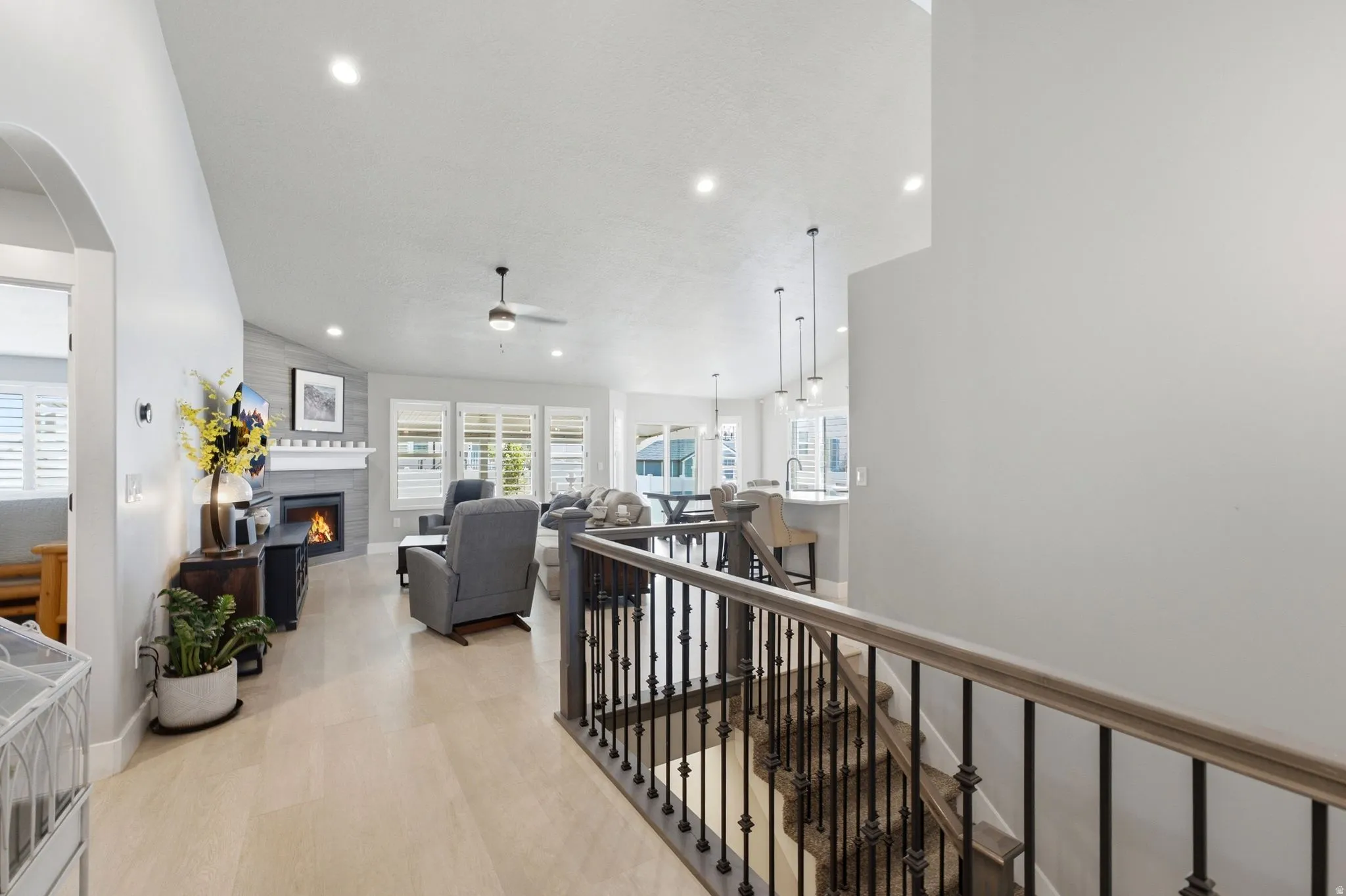 Spacious living area featuring a fireplace with a light gray surround and decorative mantel, wood-finish flooring, recessed lighting, and multiple windows with plantation shutters