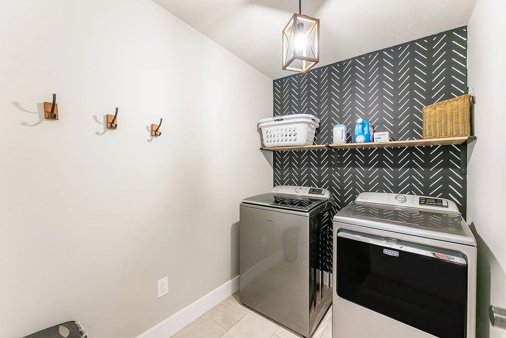 Dedicated laundry space featuring a decorative accent wall and light tile flooring