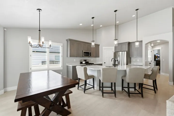 Open-concept kitchen and dining area featuring light wood-finish flooring, a kitchen island with seating, stainless steel appliances, and pendant lighting