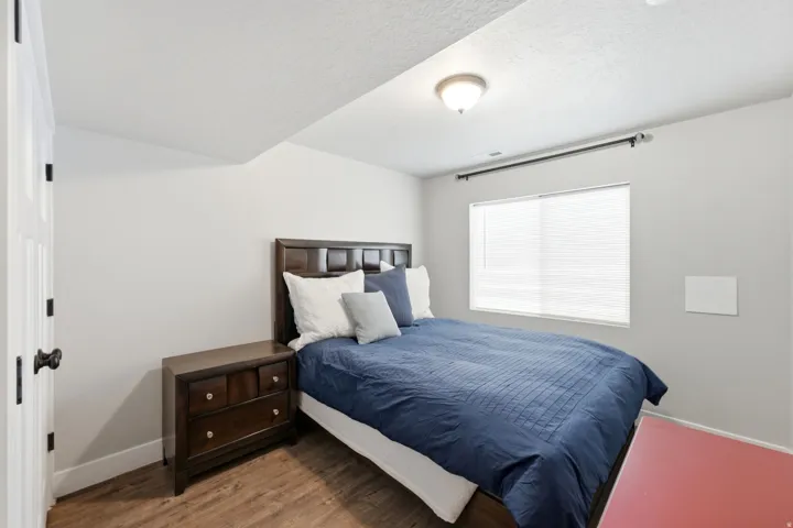 Bedroom featuring wood-finish flooring, a contemporary ceiling light fixture, a window with blinds, and white trim