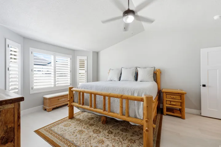 Bright room featuring light-toned flooring, plantation shutters, and a sloped ceiling with a ceiling fan