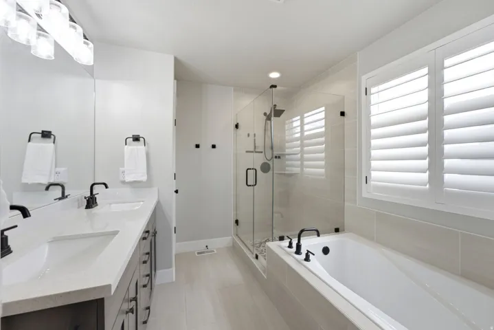 Contemporary bathroom featuring a spacious walk-in shower with a glass enclosure, a white soaking tub with matte black fixtures, and dual sinks set in a light-colored countertop