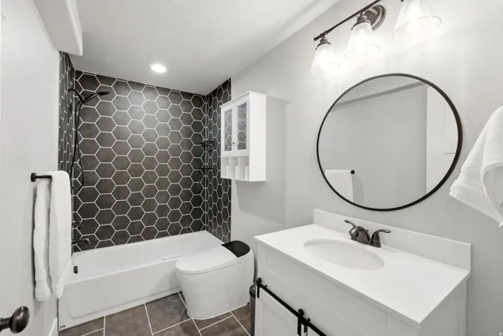 Bathroom featuring a white vanity with a white countertop, a black-framed circular mirror, and a three-light vanity fixture