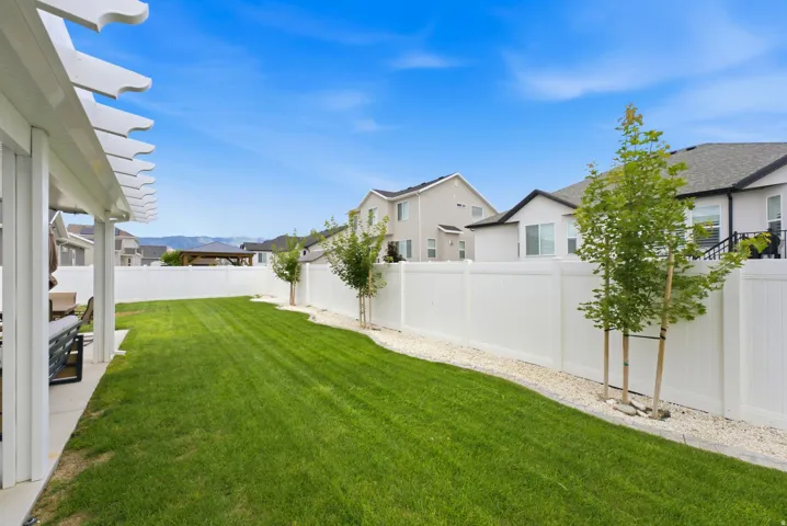 Expansive backyard featuring a manicured lawn, white privacy fencing, and a covered patio with a white pergola