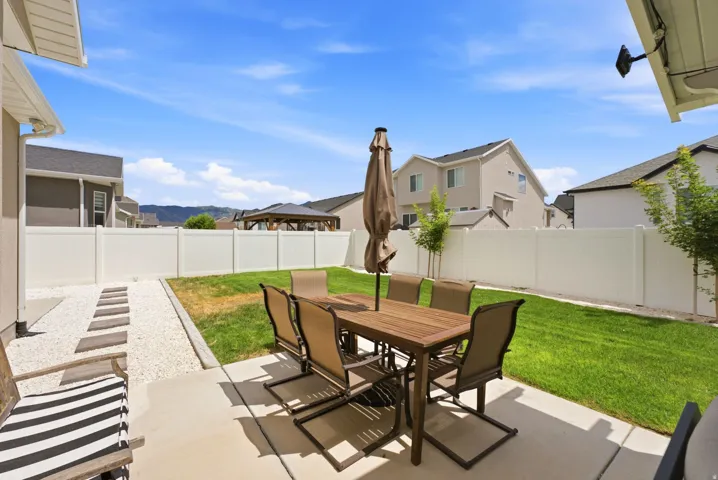 Expansive backyard featuring a concrete patio, a manicured lawn, a white privacy fence, and a gravel pathway with stepping stones