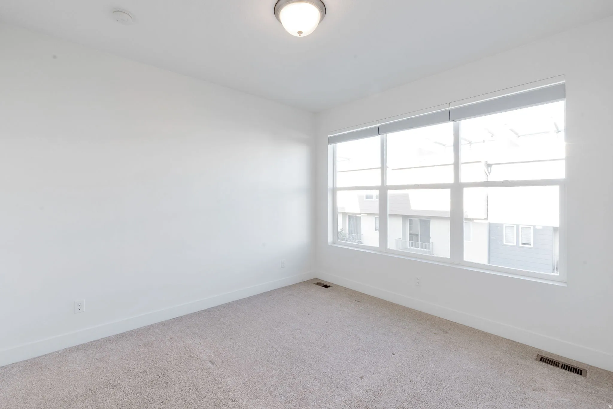 Bright room featuring large windows, neutral carpet, white walls, and a ceiling-mounted light fixture