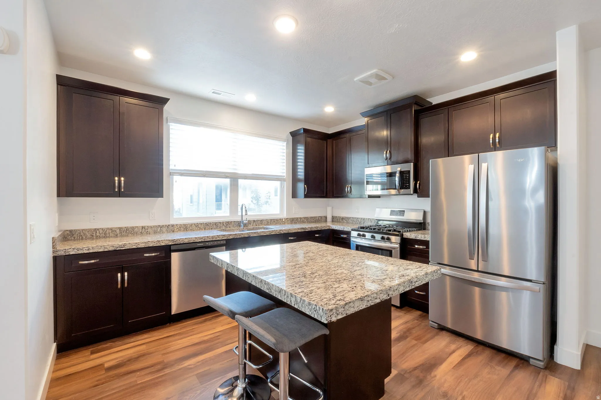 Kitchen featuring dark wood cabinetry, granite countertops, stainless steel appliances, a center island, and wood-finish flooring