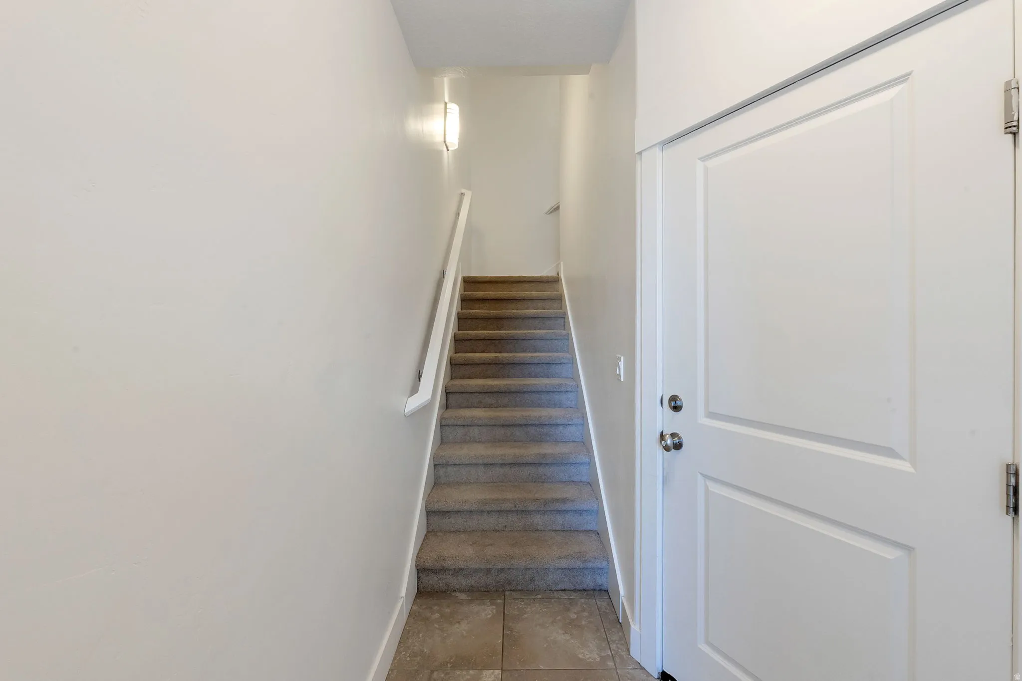 Tiled entry flooring, carpeted staircase, wall-mounted light fixture, and panel doors with chrome hardware