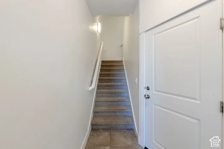 Tiled entry flooring, carpeted staircase, wall-mounted light fixture, and panel doors with chrome hardware