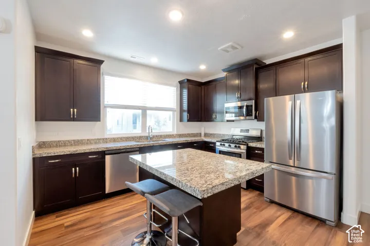 Kitchen featuring dark wood cabinetry, granite countertops, stainless steel appliances, a center island, and wood-finish flooring