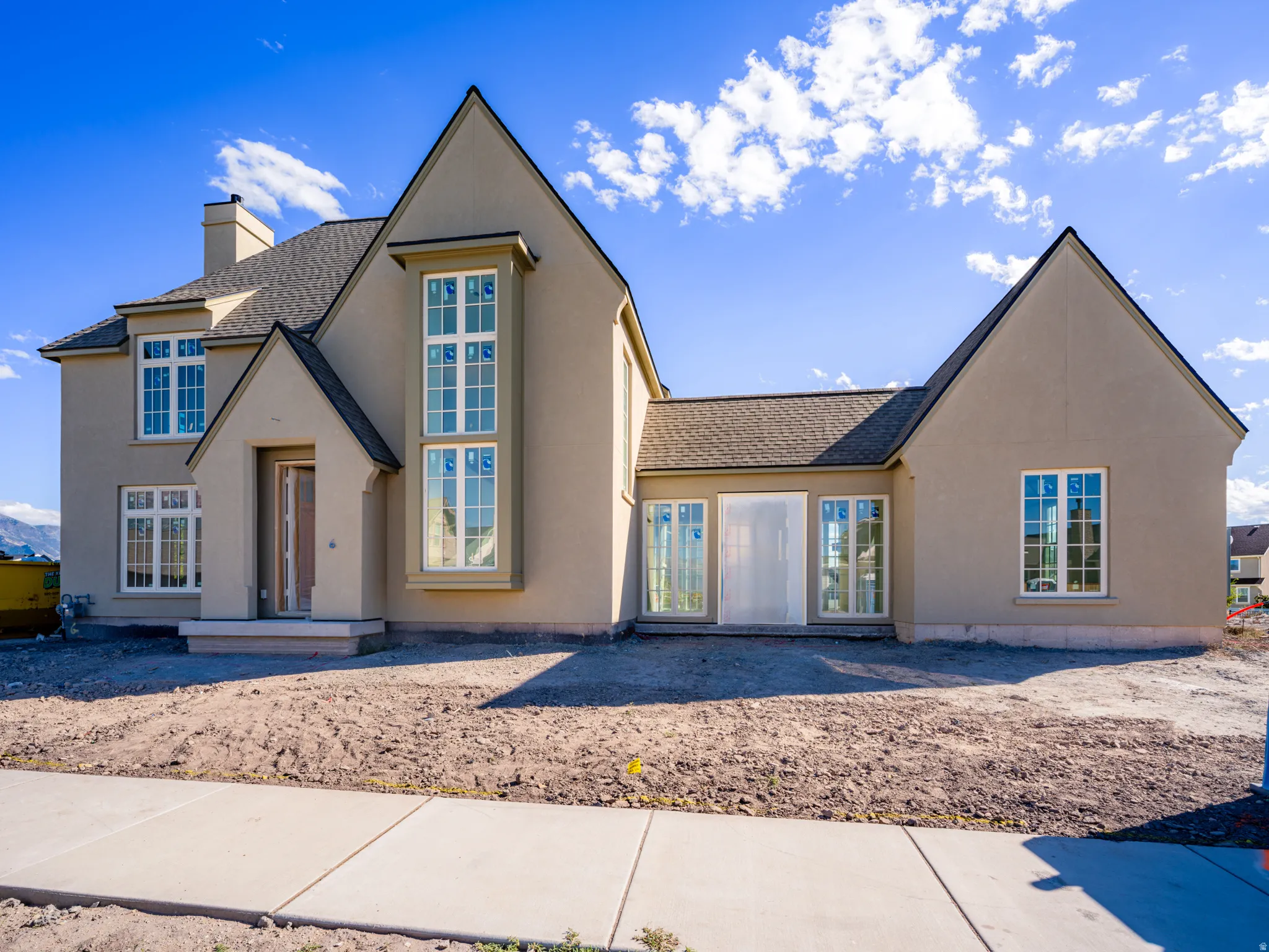 Stucco exterior featuring a prominent chimney, multiple gabled rooflines, and a covered entry with a glass-paneled door