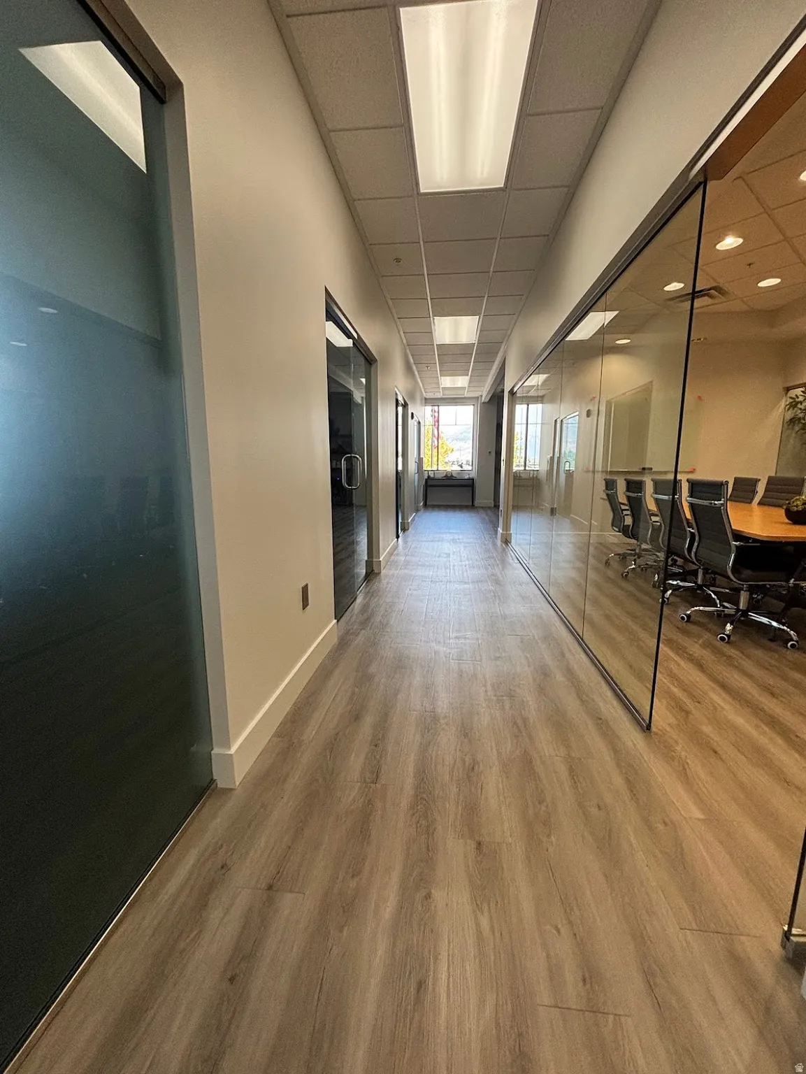 Hallway featuring wood-finish flooring, recessed ceiling lighting, and full-height glass partitions