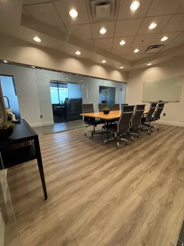 Conference room featuring glass panel walls, wood-finish flooring, a recessed ceiling with integrated lighting, and a wall-mounted whiteboard