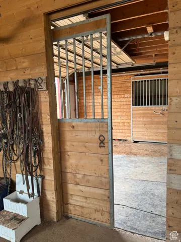 Wood-paneled stable interior featuring a sliding stall door with metal bars, exposed beam ceiling, and a concrete-finished floor