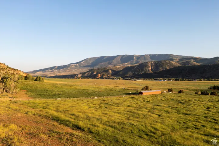 Expansive rural landscape featuring a red-roofed barn structure, open fields, and distant mountains