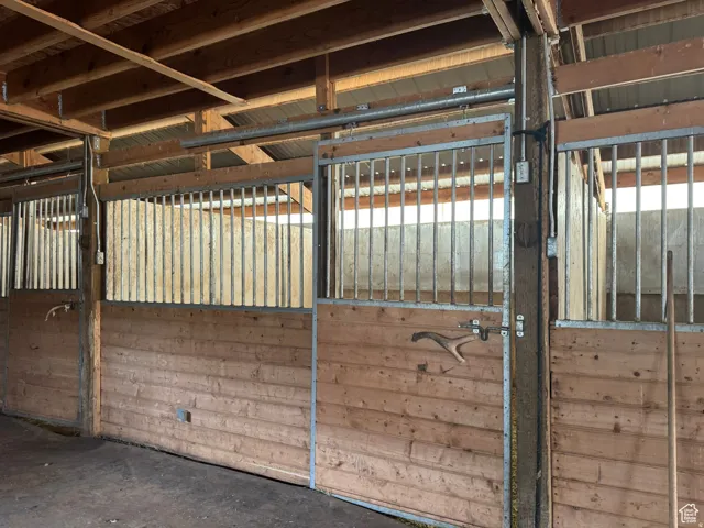 Barn interior featuring multiple stalls with wood paneling and metal bar upper sections