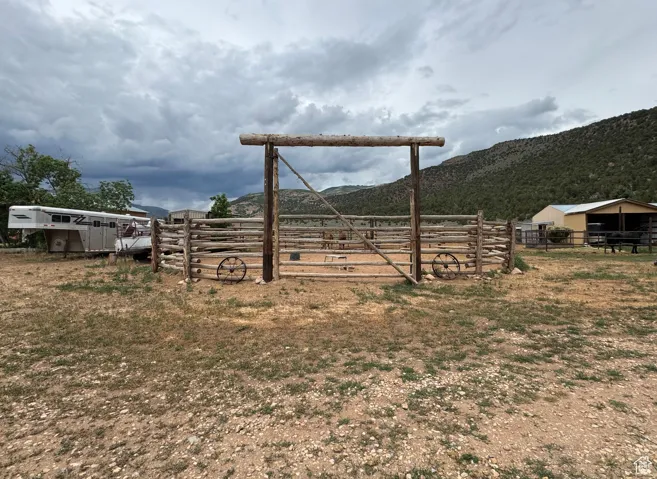 Wood-fenced round pen with a log entrance, situated on a sprawling unlandscaped lot with a distant mountain backdrop and a barn structure