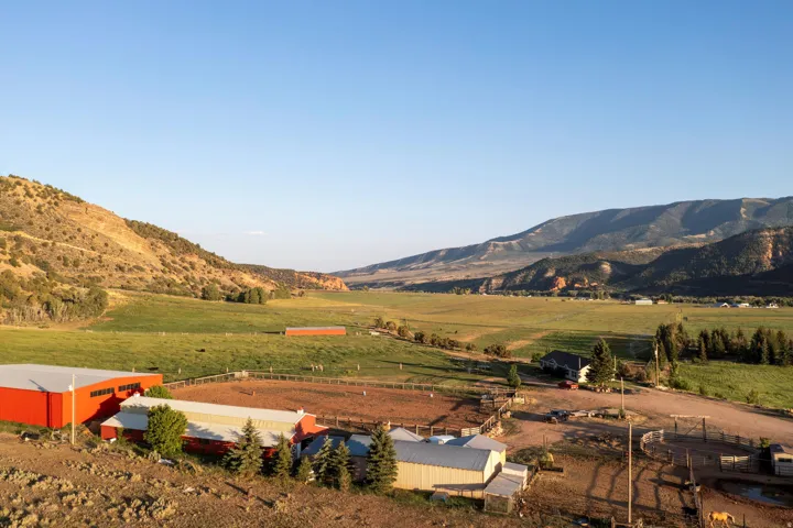 Expansive property featuring multiple outbuildings, fenced corrals, a large red barn, and a single-family residence, all set against a mountainous backdrop