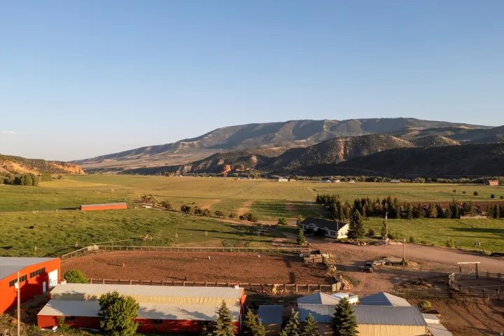 Expansive property featuring an equestrian arena, multiple barns, and a residence, all set against a backdrop of rolling hills and distant mountains