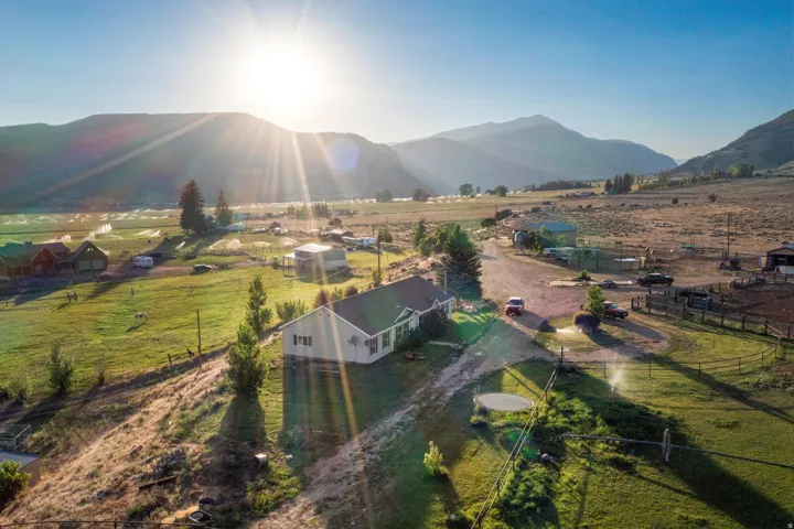 Sprawling property featuring a single-story residence with a gabled roof, an expansive unpaved driveway, and a partially fenced perimeter