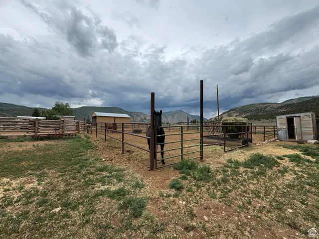 Expansive fenced pastureland featuring a hay feeder, multiple outbuildings, and mountain backdrops