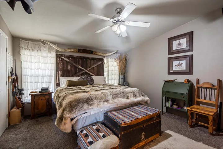 Bedroom featuring a ceiling fan, plush carpeting, window with layered white curtains, and neutral wall paint