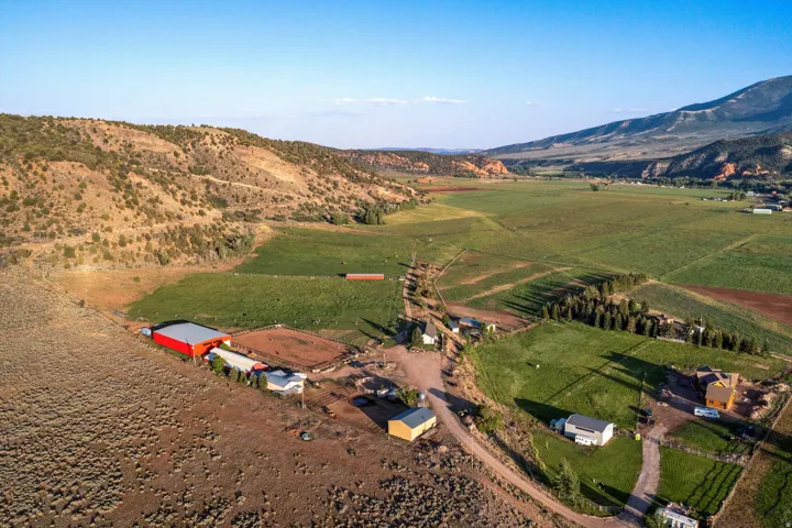 Expansive rural property featuring multiple structures, including a large red barn with an adjacent riding arena, several residential buildings, and extensive green pastures