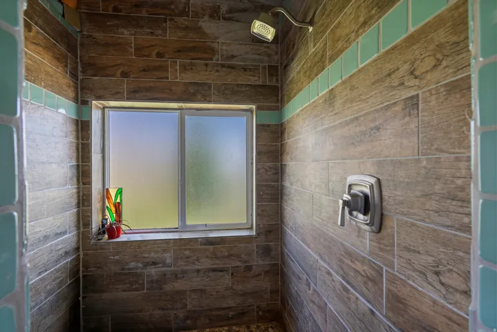 Shower enclosure featuring wood-finish tile walls with a teal accent band, a frosted window, and a brushed nickel shower head and control