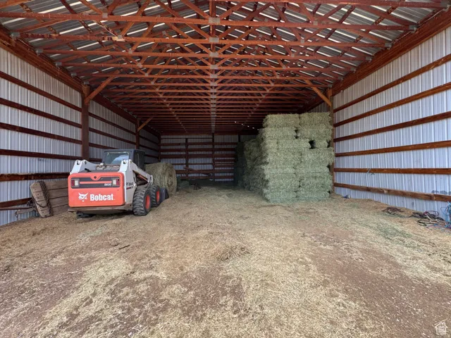 Spacious barn structure featuring a metal roof, exposed wood beam framing, corrugated metal siding, and an open dirt floor