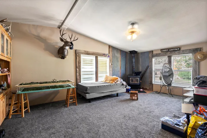 Spacious room featuring sloped ceilings, two windows with blinds, and a built-in wood-burning stove with a corrugated metal accent wall