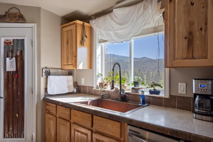 Kitchen featuring a window offering mountain scenery, a copper-tone sink with a gooseneck faucet, light wood cabinetry, and a dark tile backsplash