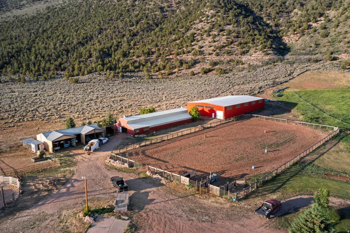 Expansive equestrian property featuring a fenced riding arena, multiple outbuildings, and a large red barn