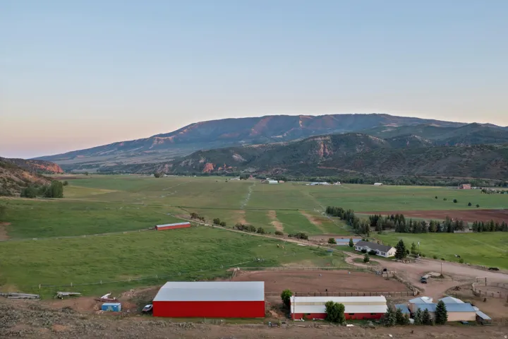 Expansive property featuring multiple outbuildings, including a large red barn with a light-colored roof, a smaller red and white barn, and several utility structures