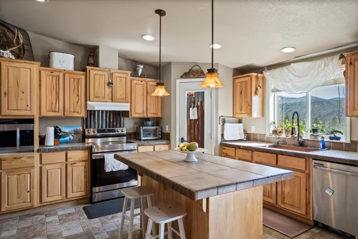 Kitchen featuring natural wood cabinetry, a central island with a tile countertop, and stainless steel appliances