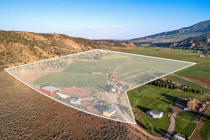 Expansive property featuring a red agricultural structure, multiple outbuildings, and cultivated land