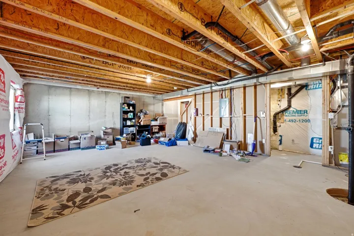 Unfinished basement featuring exposed wood joists, concrete foundation walls, and framed interior walls