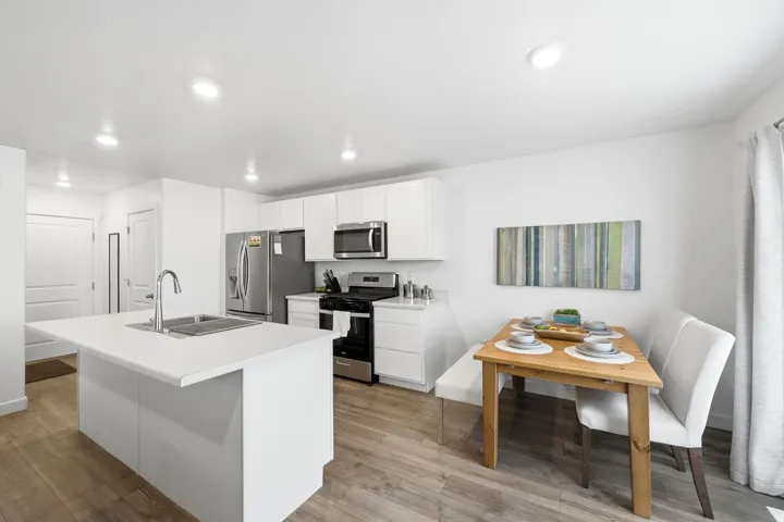 Modern kitchen featuring a white island with an undermount sink, stainless steel appliances, white cabinetry, wood-finish flooring, and recessed lighting
