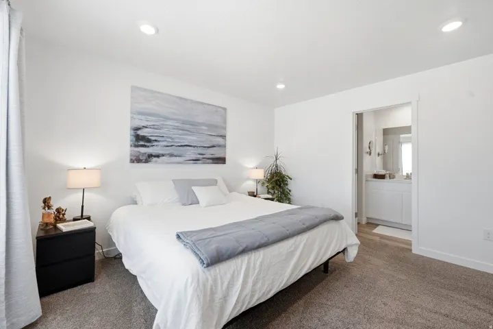 Spacious bedroom with plush carpeting, recessed lighting, and a private ensuite bath featuring a single vanity and mirrored medicine cabinet