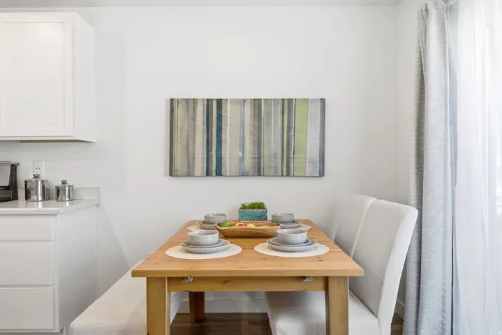 Dining area featuring a wood-finish table, built-in upholstered bench seating, and a window with sheer and patterned curtains
