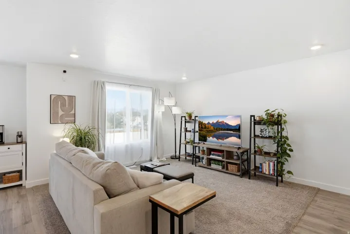 Living area featuring recessed lighting, a large window with sheer and blackout curtains, and wood-finish flooring extending to a carpeted section