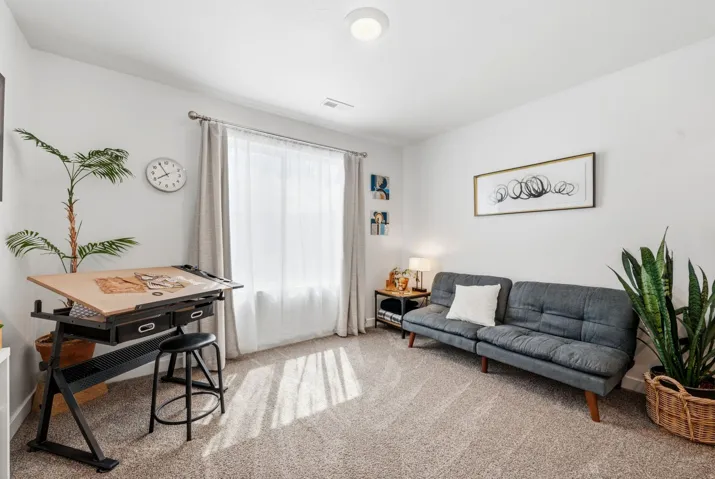 Bright interior space featuring a large window with drapes, light neutral carpeting, white walls, and a flush-mount ceiling light